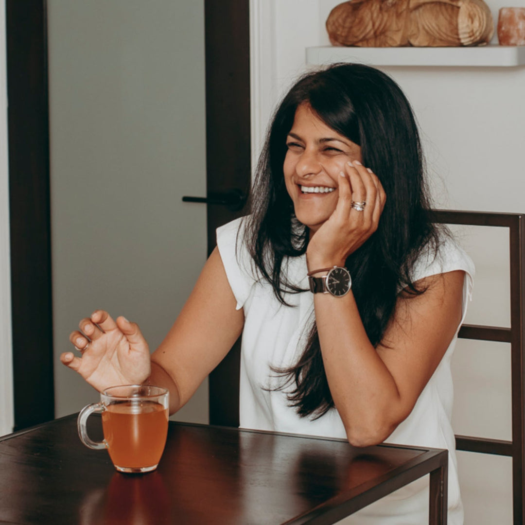 Woman sitting at a table with a mug of tea, smiling.