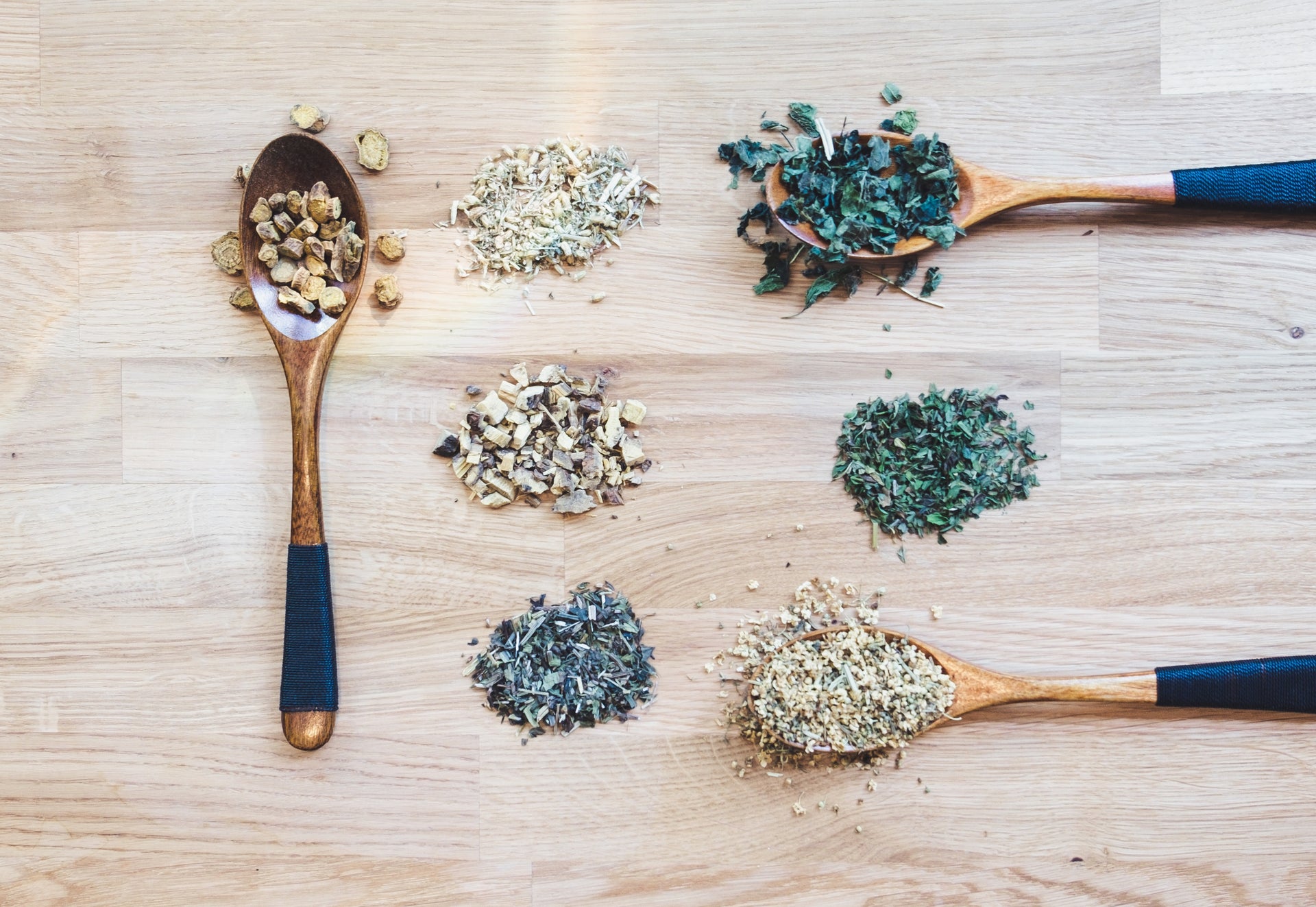 Wooden spoons with various dried herbs on a wooden surface